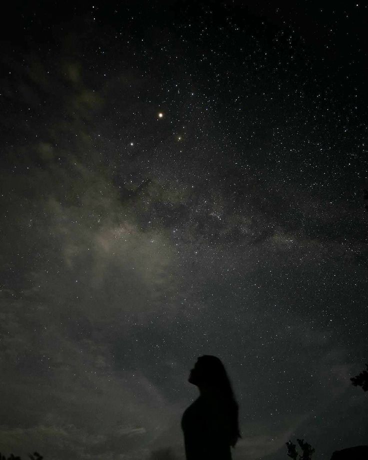 a person standing in the dark looking up at the night sky with stars above them