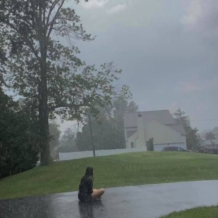 a person sitting in the rain with an umbrella over their head, on a rainy day