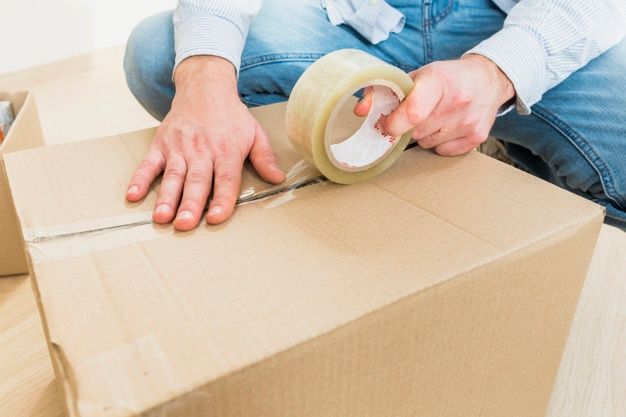 a man sitting on top of a cardboard box with tape around his ankles and hands