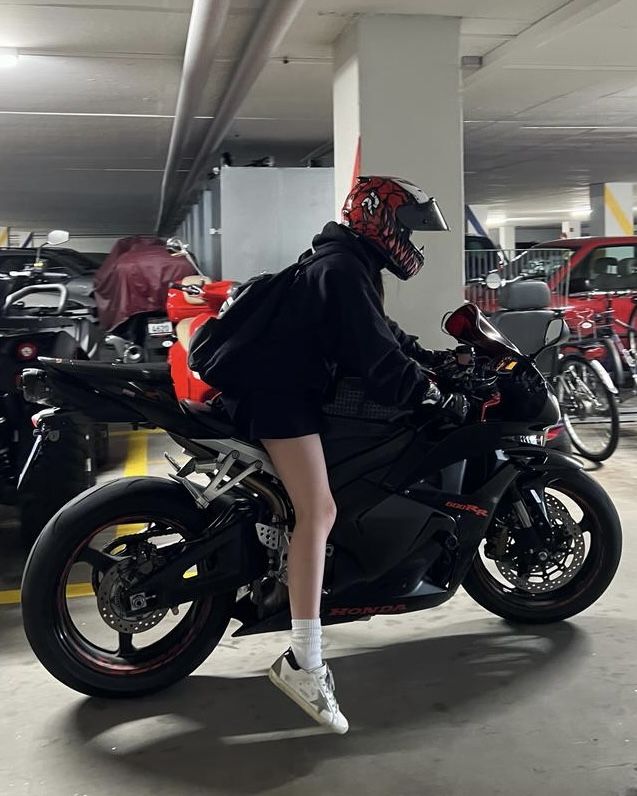 a person sitting on a motorcycle in a parking garage with other cars and motorcycles behind them