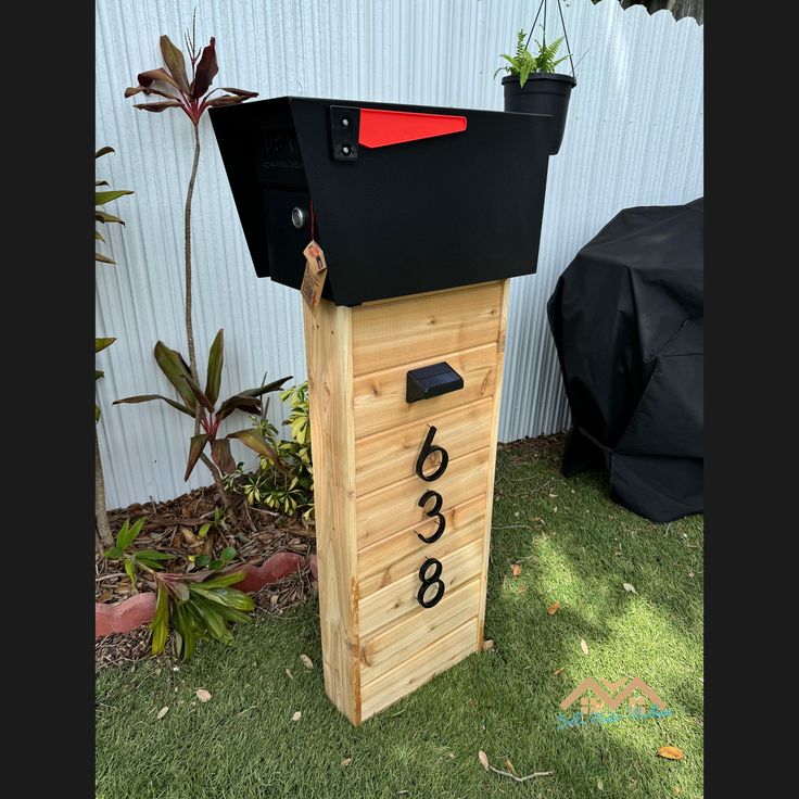 a mailbox sitting in the grass next to a fence with plants growing out of it