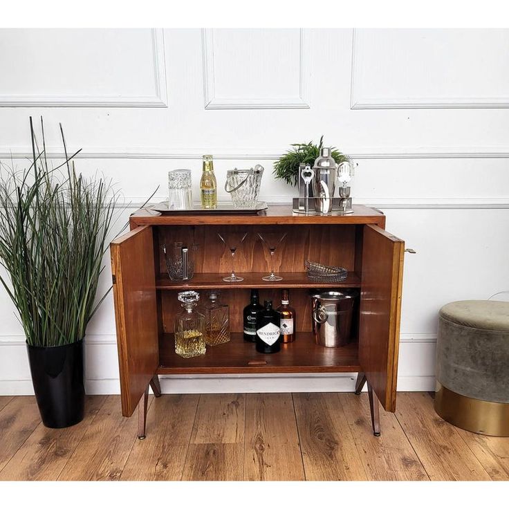 a wooden cabinet filled with bottles and glasses next to a potted plant on top of a hard wood floor