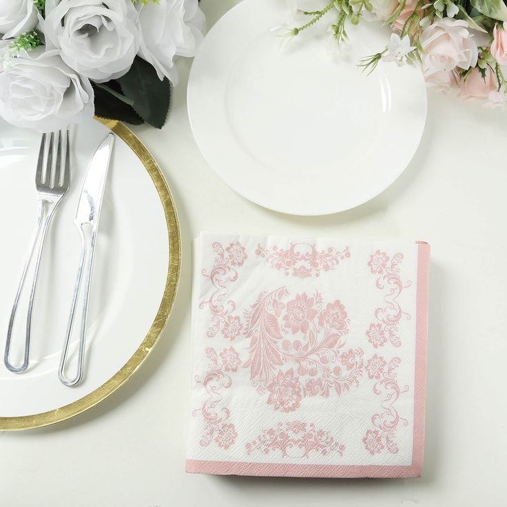 a place setting with pink and white napkins, silverware and flowers on the table