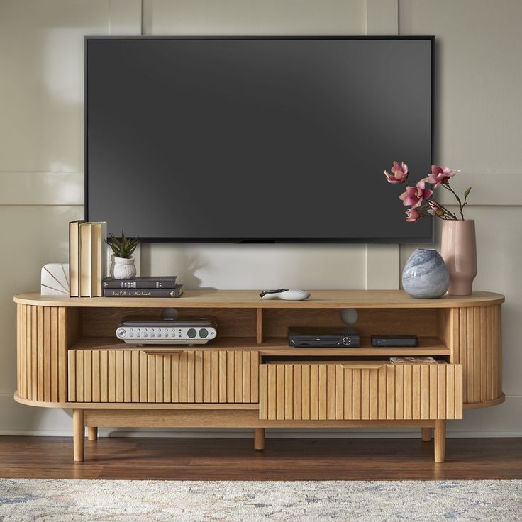 an entertainment center with a flat screen tv mounted on it's wall and two vases filled with flowers