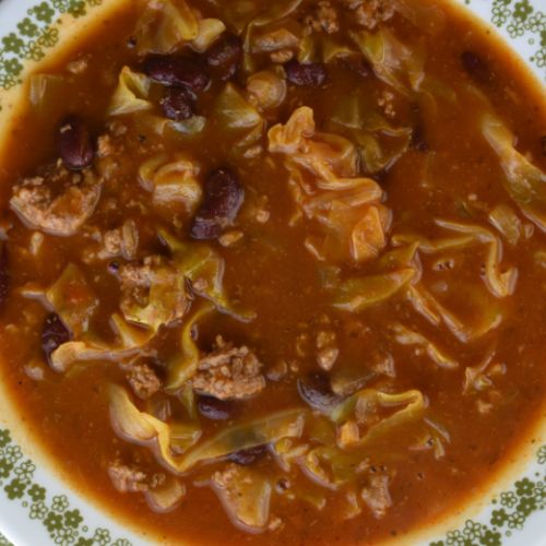 a bowl of soup with meat and vegetables on a green and white tableclothed plate