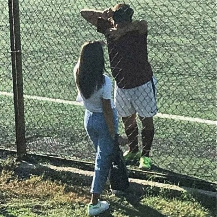 two people standing in front of a fence with their arms around each other and one person holding a tennis racquet