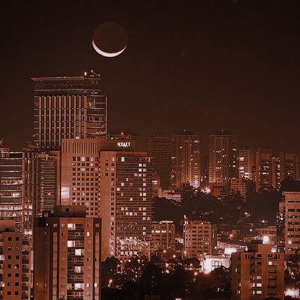 the moon is setting over a city skyline at night with buildings lit up in the foreground