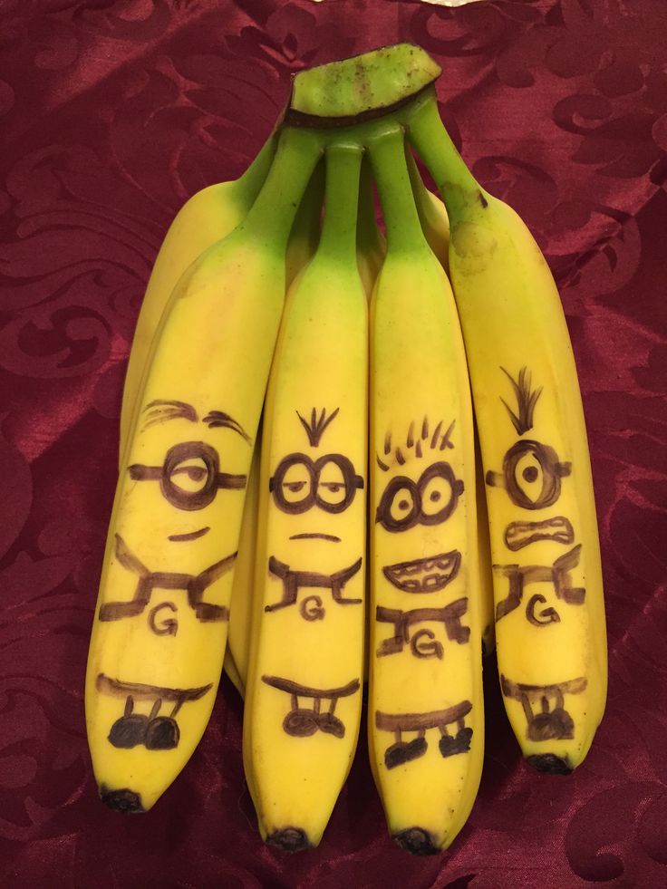 five bananas with faces drawn on them sitting on a red tableclothed surface,