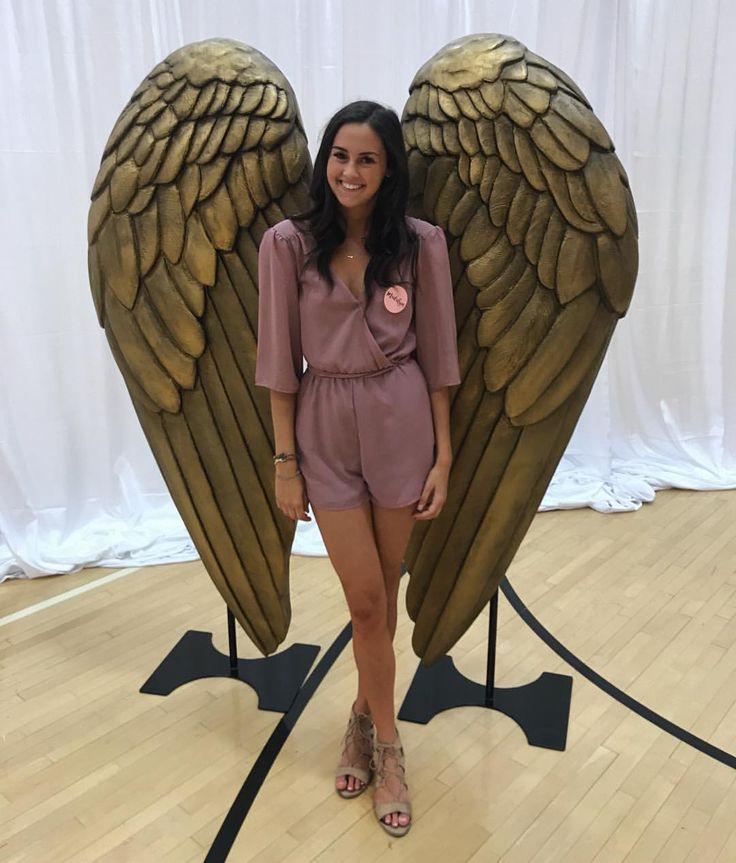 a woman standing in front of an angel wings display on a wooden floor with white curtains behind her