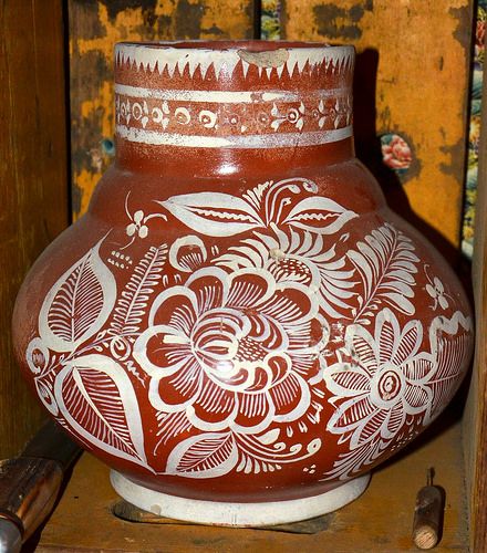 a red and white vase sitting on top of a wooden shelf next to a hammer