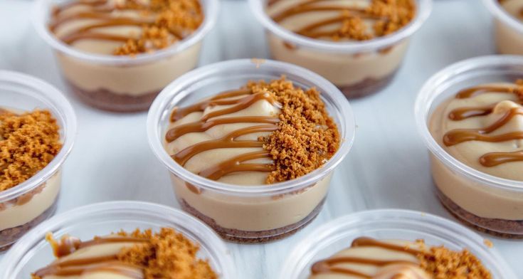 several desserts in plastic cups with caramel drizzled on the top