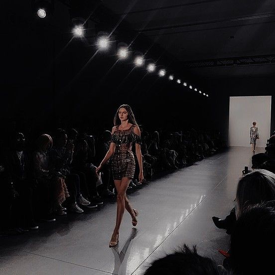 a woman walking down a runway in front of a group of people wearing dress clothes