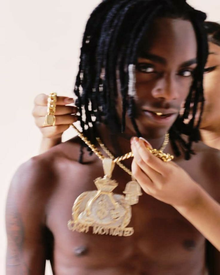 a young man with dreadlocks is holding up a gold necklace that has an emblem on it