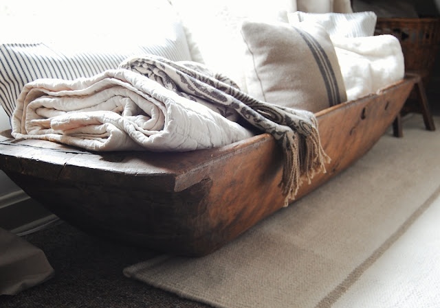 an old wooden boat is sitting on the floor in front of a window with pillows and blankets