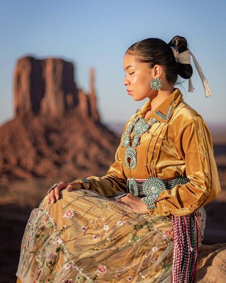 a woman sitting on top of a rock in front of a desert landscape with a mountain in the background