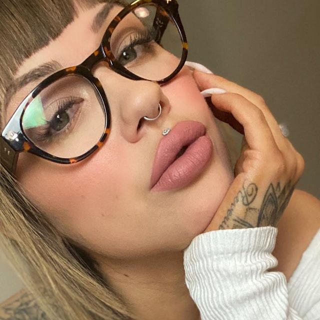 a close up of a person wearing glasses with tattoos on her arm and hand near her face