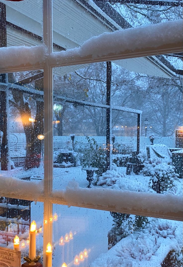 candles are lit in front of a window as it snows