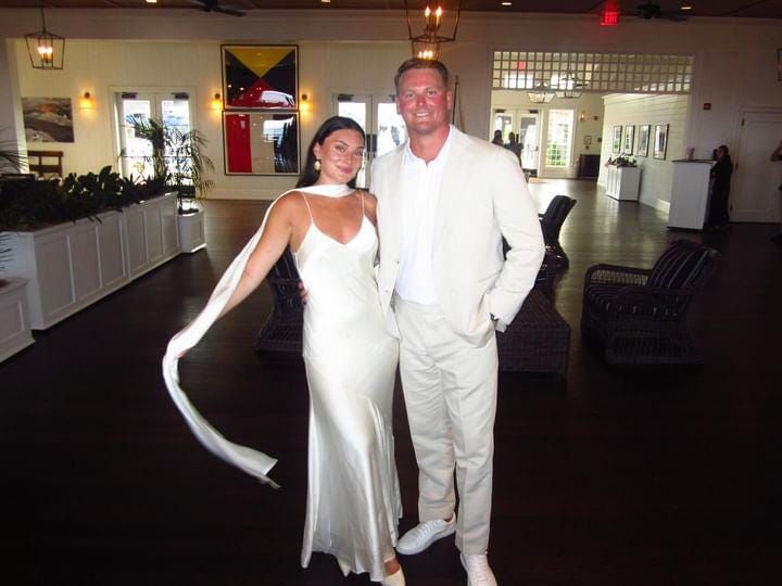 a man and woman posing for a photo in formal wear at an event with white decor