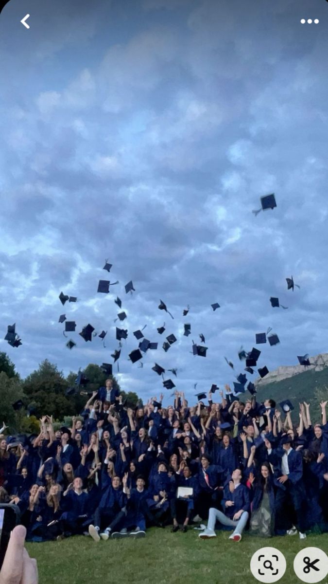 a large group of graduates throwing their caps in the air at graduation ceremony on a cloudy day