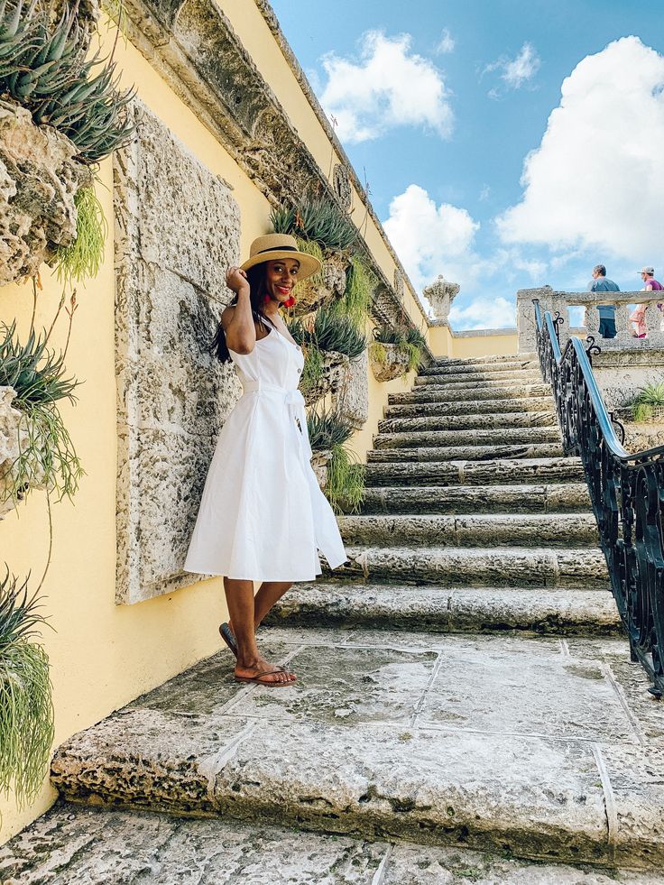 a woman in a white dress and straw hat standing on steps