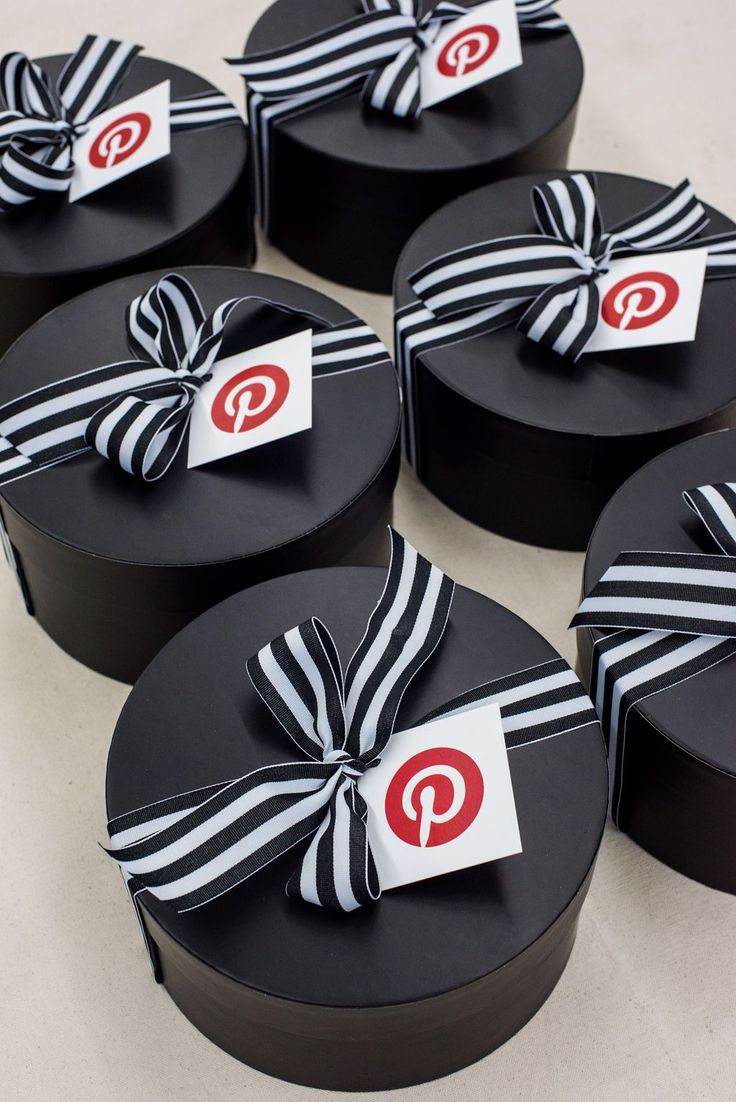 six black round boxes with white and red ribbons tied around the top one has a pin logo on it