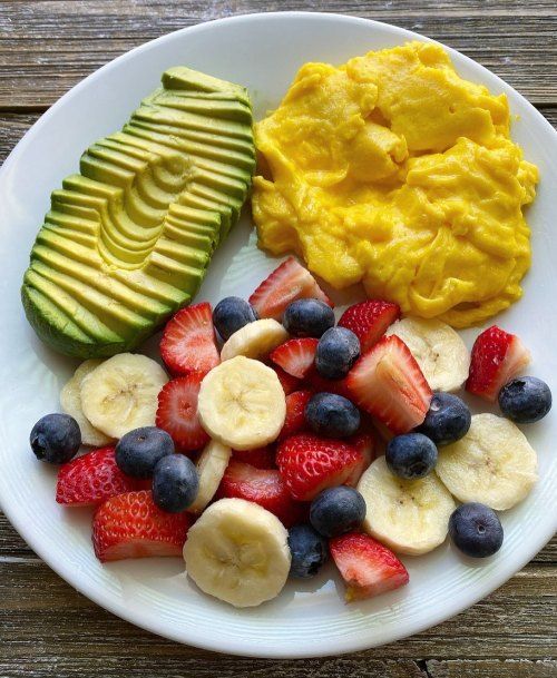 a white plate topped with fruit next to an avocado and sliced strawberries