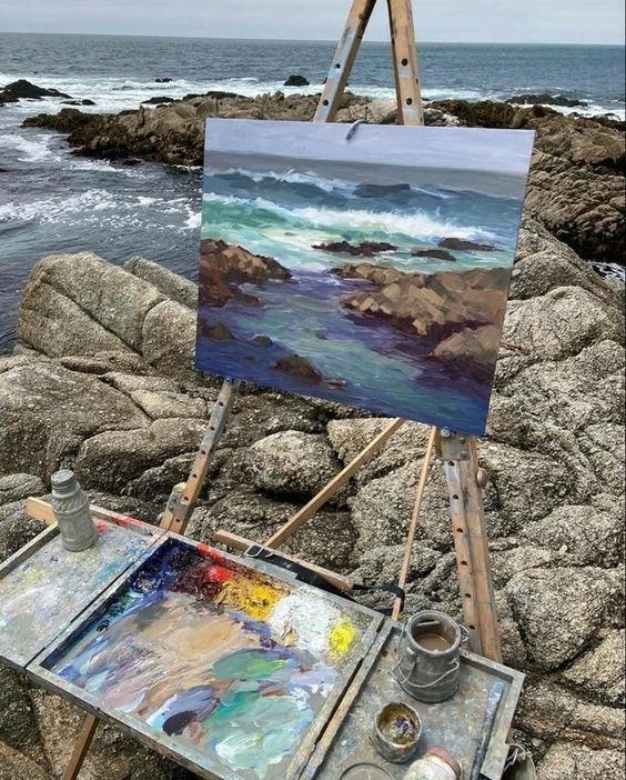 an artist's easel with paint and watercolors on it near the ocean