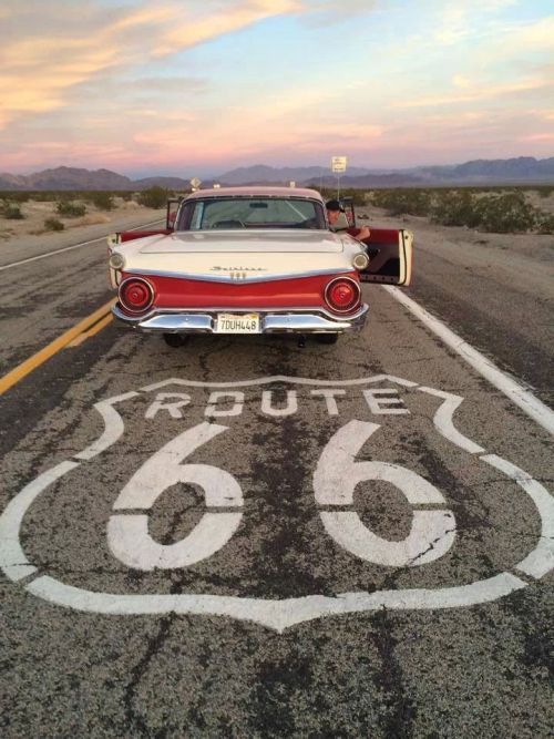 an old red and white car sitting in the middle of a road with route 66 painted on it