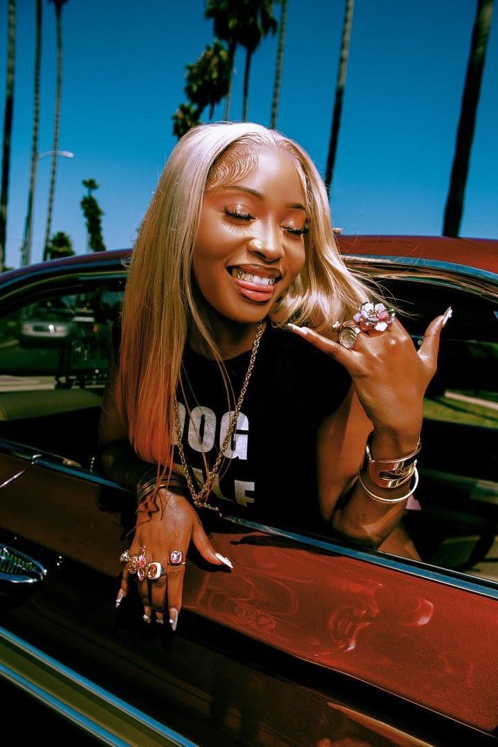 a woman leaning out the window of a car with palm trees in the background and her hand up to her face