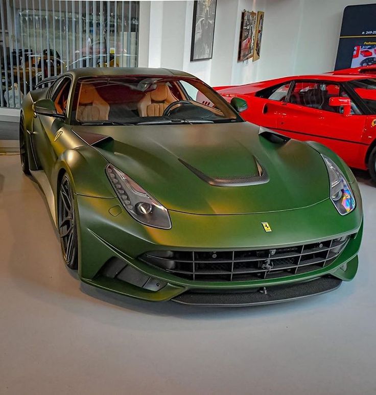 two green sports cars in a showroom with red one behind them and another on the other side