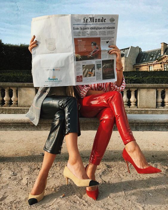 a woman sitting on a bench reading a newspaper while wearing red pants and high heels