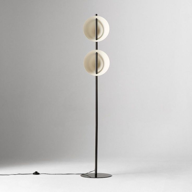 three lights on a metal pole in front of a white wall with a black floor lamp