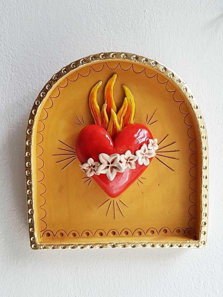 a decorative heart shaped dish with flowers and leaves on the side, mounted on a wall