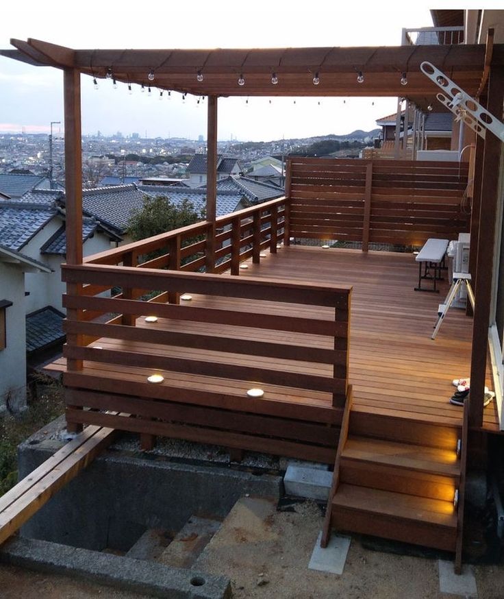 a wooden deck with stairs leading up to it and lights hanging from the roof above