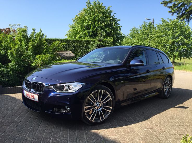 a blue bmw car parked on the side of a road next to bushes and trees