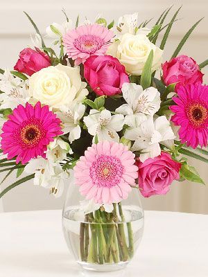 a vase filled with pink and white flowers sitting on top of a table next to a phone