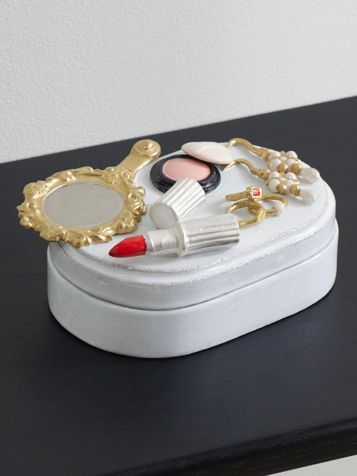 there is a small white box with makeup on it and gold trim around the lid