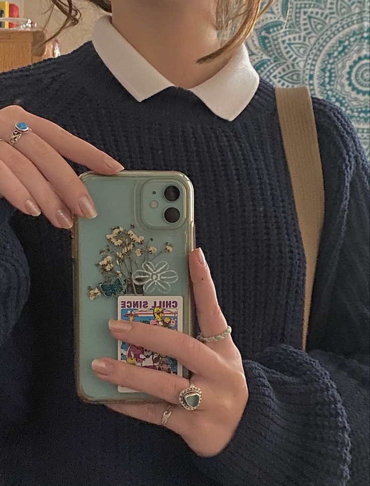 a woman is holding up her phone case that has flowers on it and she's wearing gold rings