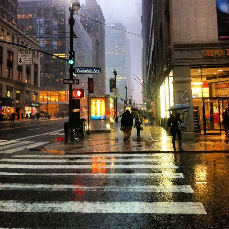 people crossing the street at an intersection on a rainy day with buildings in the background