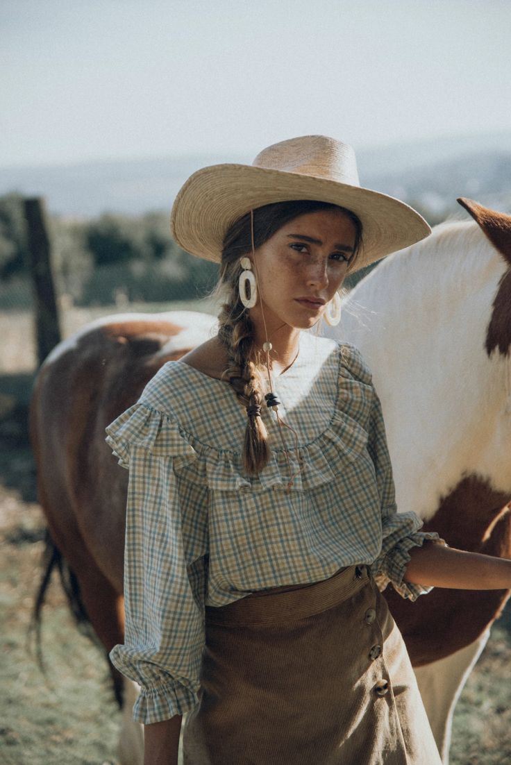 a woman standing next to a brown and white horse wearing a hat on her head