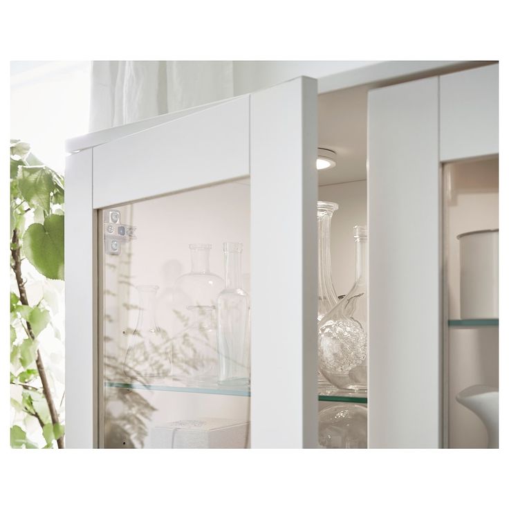 an open cabinet with glassware in it next to a potted plant and vases