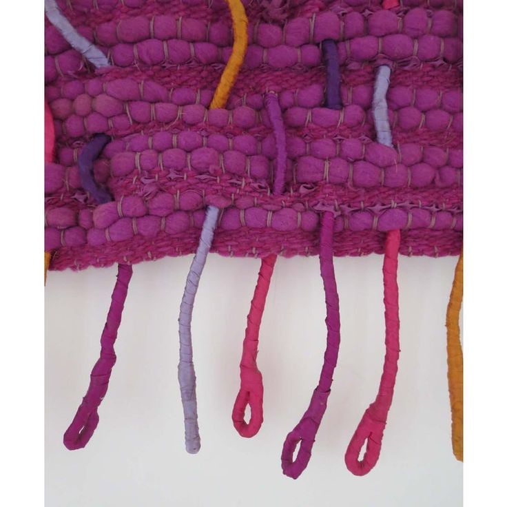 some purple and orange yarns hanging on a white wall with one knot in the middle