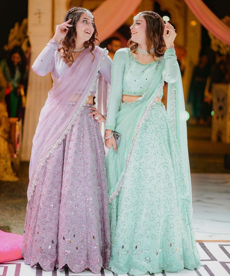 two young women dressed in pastel colored lehenga's standing next to each other