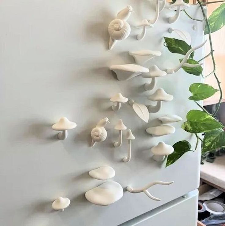 there are many white mushrooms on the wall next to a potted plant in front of a refrigerator