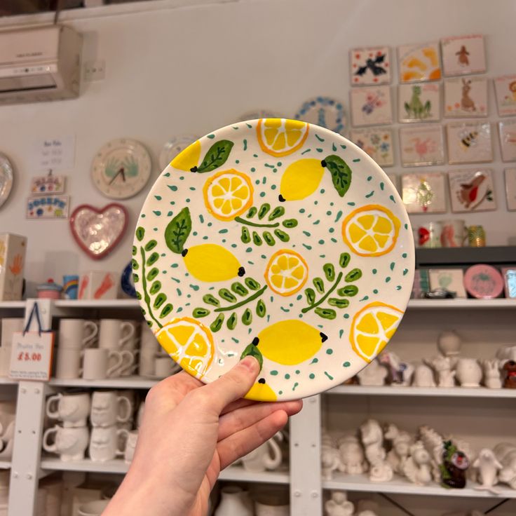 a hand holding a plate with lemons on it in front of shelves full of plates