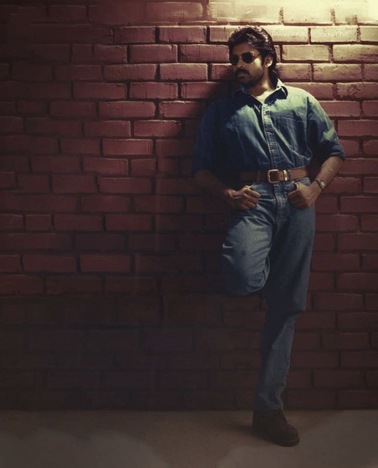 a man leaning against a brick wall with his hands on his hips