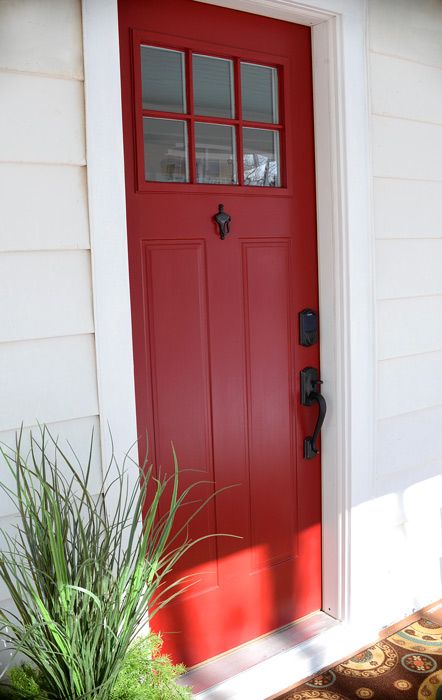 a red front door on a white house with potted plants in the foreground