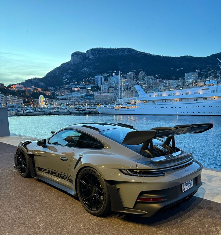 a grey sports car parked in front of a large body of water