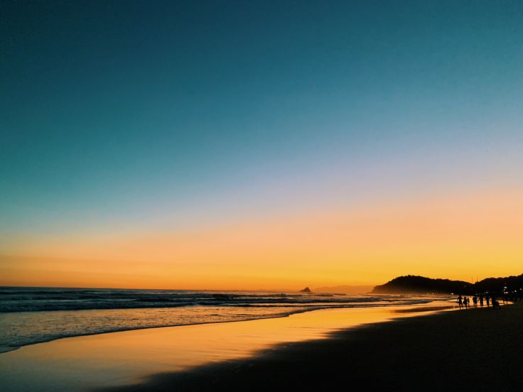 people are walking on the beach at sunset