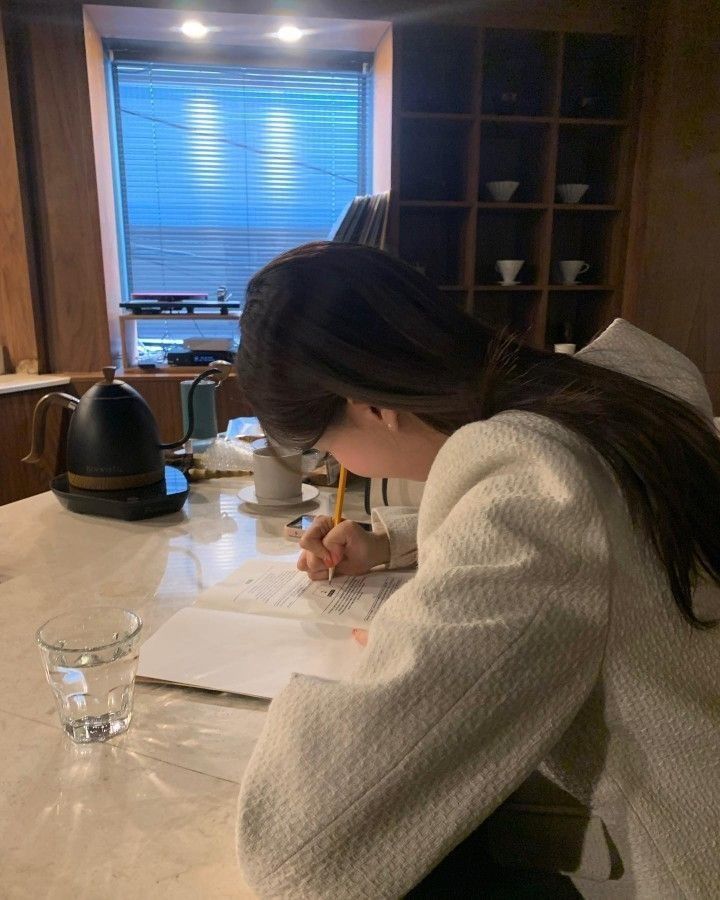 a woman sitting at a kitchen counter writing on a piece of paper with a pencil